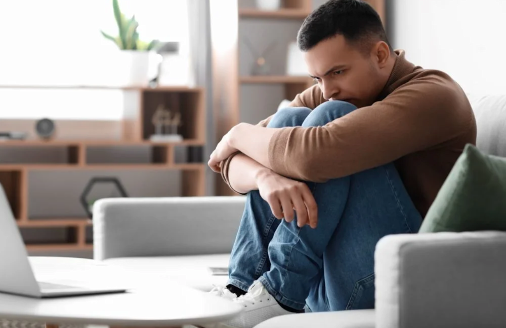 man sitting on couch, lost in thought, suffering from alcohol addiction